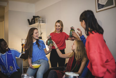 Happy friends holding beer bottles while enjoying at living room