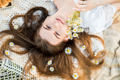 High angle portrait of woman lying on bed while holding flowers