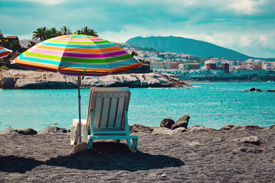 Deck chairs on beach by sea against sky