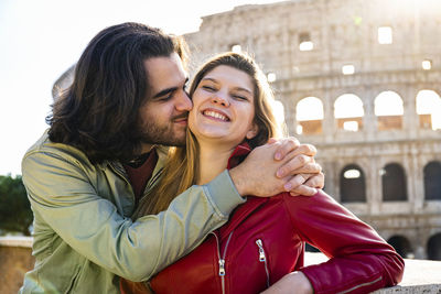 Young couple traveling to rome. the couple is kissing in front of the colosseum.