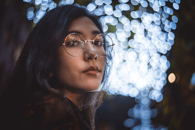 Portrait of smiling young woman standing by illuminated light at night