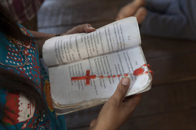 Midsection of woman praying with book and rosary beads at chapel