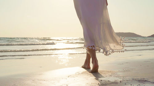 Low section of woman on beach against sky