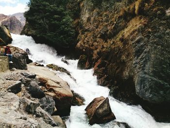 Woman sitting by stream flowing through rocks
