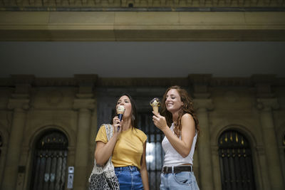 Young women eating ice cream while standing against building