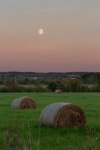 Hay bales on field against sky during sunset