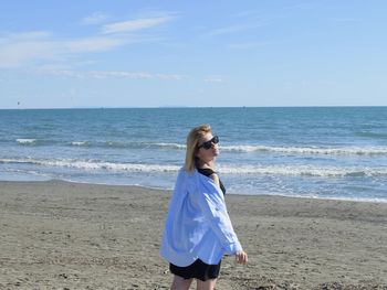 Rear view of woman standing at beach against sky