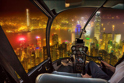 Midsection of pilot flying helicopter over illuminated city at night