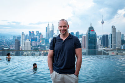 Man standing by swimming pool against buildings in city