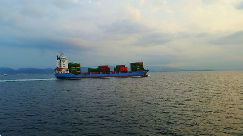 Container ship sailing in sea against sky during sunset