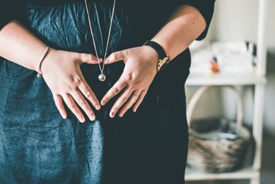 Midsection of pregnant woman making heart shape on abdomen