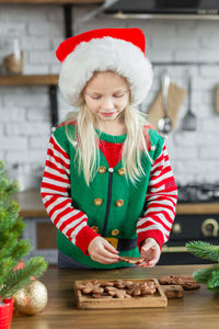 Girl in santa hat cooking, decorating gingerbread cookies