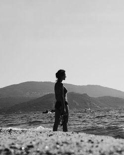 Woman looking at sea against clear sky and mountain background