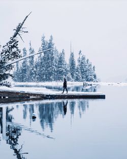 Man by lake on jetty against clear sky during winter