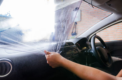 Cropped hands of woman removing plastic from car windshield