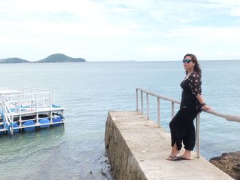 Woman standing on railing by sea against sky