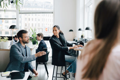 Businessman showing smart phone to female colleague while working at coworking space