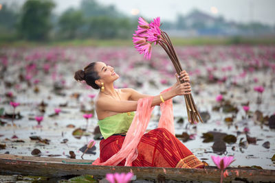Young woman holding water lilies sitting in boat on lake