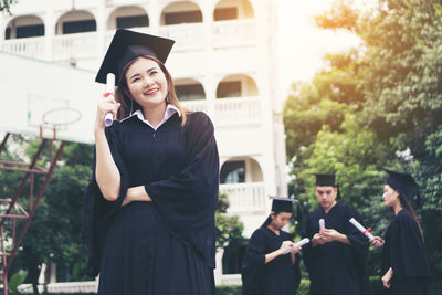 Cheerful student in graduation gown standing outdoors