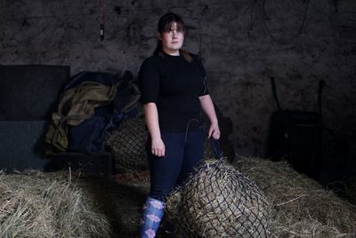 Portrait of woman standing by hay in net against wall