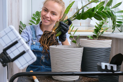 Gardener woman blogger using phone while transplants indoor plants and use a shovel on table. 