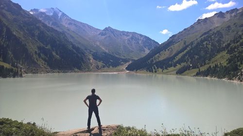 Rear view of shirtless man standing on lake against mountains