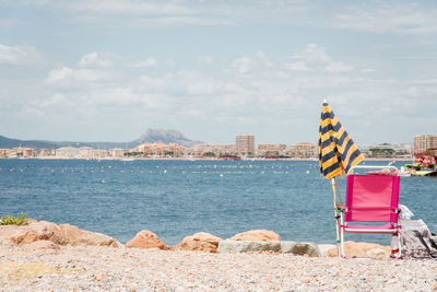 Umbrella and chair on beach against buildings in city