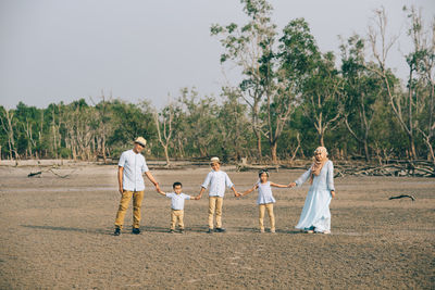 Portrait of happy family holding hands while standing at beach against sky