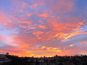 Silhouette city against dramatic sky during sunset