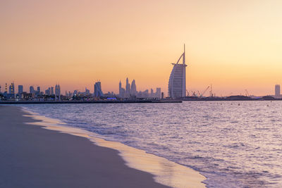 Sea by buildings against sky during sunset