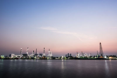 Illuminated factory by river against sky at night