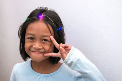 Portrait of smiling girl with illuminated lighting on head gesturing against wall