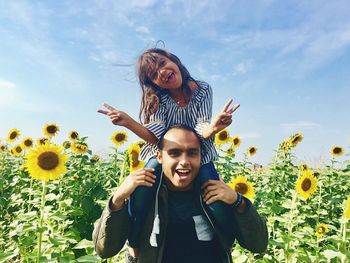 Cheerful father carrying daughter on shoulder while standing in sunflower field