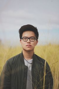 Portrait of young man standing on field against sky