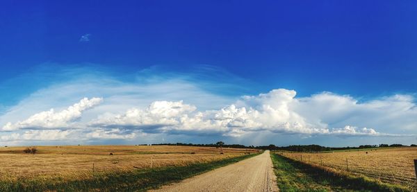 Empty road amidst agricultural field against blue sky