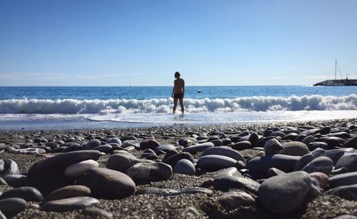 Rear view of person standing at beach against clear blue sky