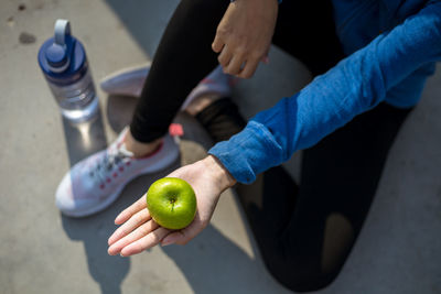 Low section of woman holding apple whiles sitting outdoors