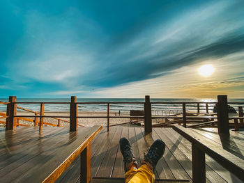 Low section of people by sea against sky during sunset