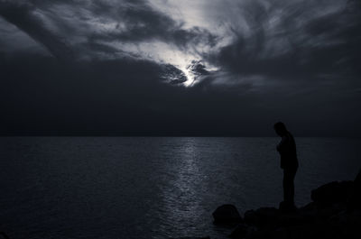 Silhouette man standing in sea against sky