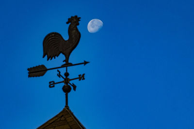 Low angle view of weather vane against blue sky