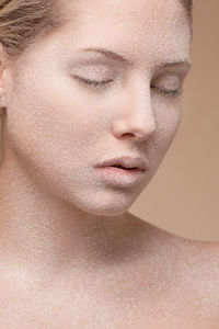 Close-up of young woman with powder on face against brown background