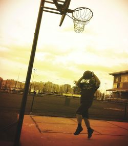 Man standing by basketball hoop against sky during sunset