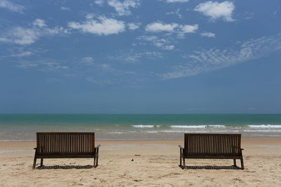 Deck chairs on beach against sky