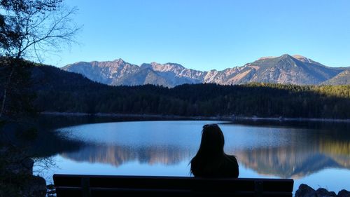 Rear view of silhouette woman sitting on bench by lake