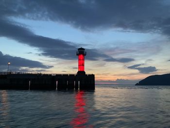 Lighthouse by sea against sky during sunset