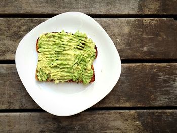 High angle view of avocado and bread in plate on wooden table