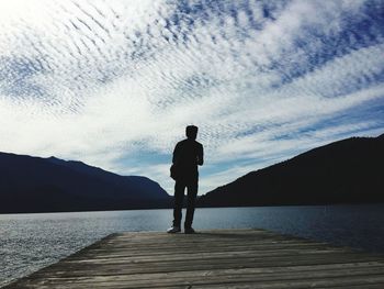 Silhouette man standing on jetty by lake against sky