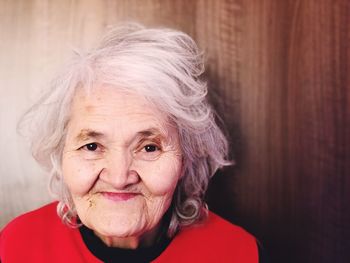 Close-up portrait of smiling senior woman against wall