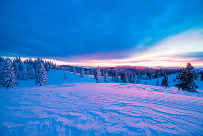 Snow covered landscape against cloudy sky during sunset