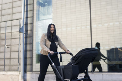 View of smiling mid adult woman on parental leave pushing pram